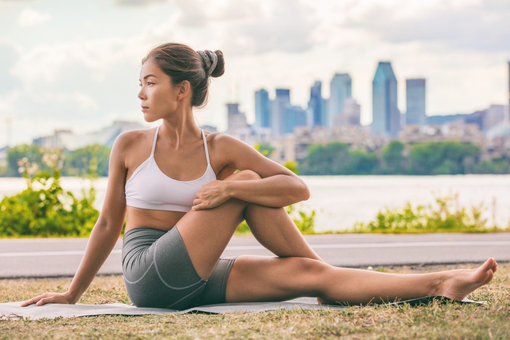 Yoga stretch exercise fit Asian woman stretching lower back for spine health on city outdoor fitness class in park. Seated spinal twist.